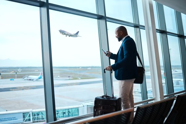 black man with phone, airport window and plane taking off, checking flight schedule terminal for business trip. technology, travel and businessman reading international travel restrictions app online