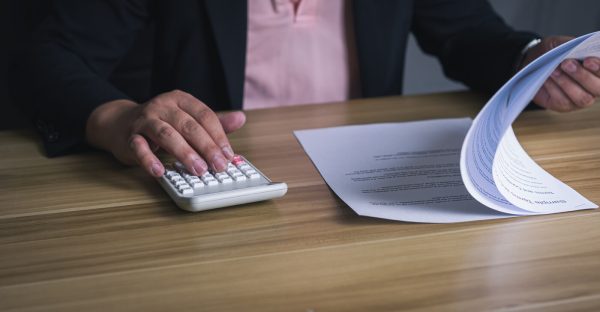 businessman using calculator and reviewing financial documents at desk. concept of accounting, finance, auditing, tax, and business analysis.
