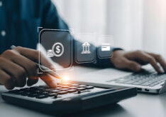 person using a calculator and laptop with currency, bank, and credit card digital icons, analyzing finances and managing banking online.