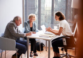 senior couple signing document in meeting with female financial advisor in office