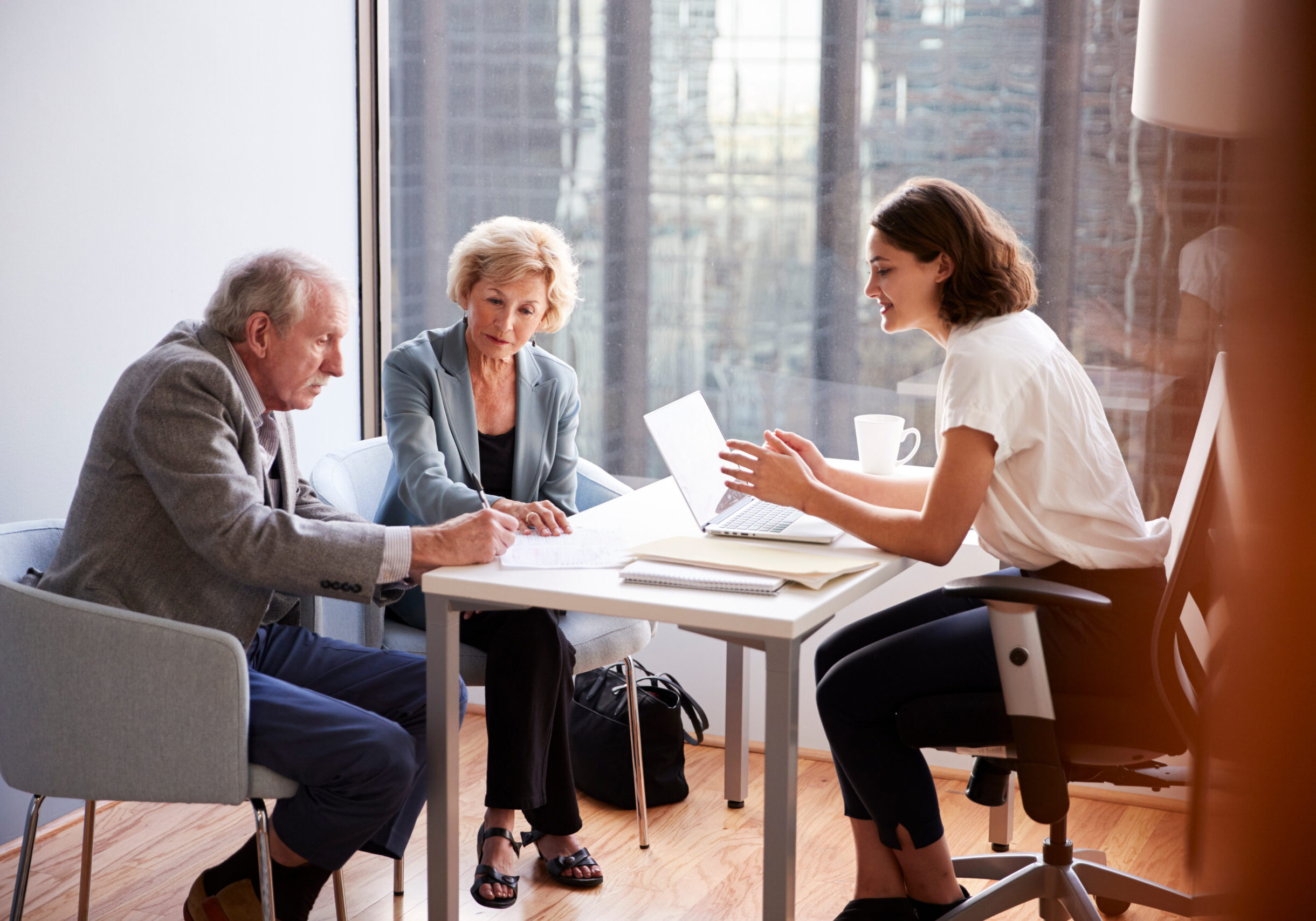 senior couple signing document in meeting with female financial advisor in office