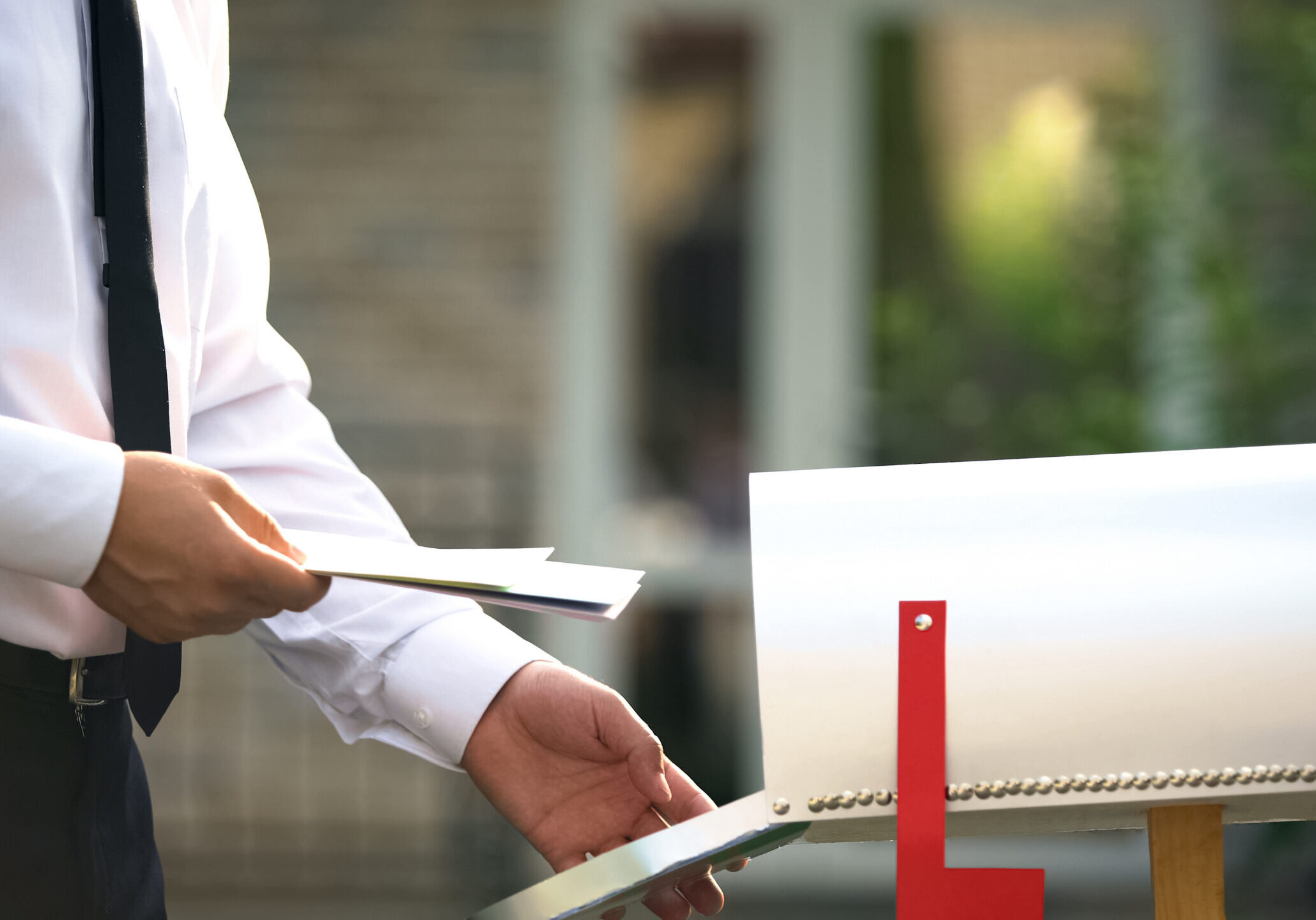 businessman sending letters and bills, putting them into mailbox near house