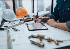 engineering working with drawings inspection on tablet in the office and calculator, triangle ruler, safety glasses, compass on blueprint. engineer, architect, industry and factory concept.