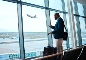 black man with phone, airport window and plane taking off, checking flight schedule terminal for business trip. technology, travel and businessman reading international travel restrictions app online