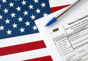 form 990 return of organization exempt from income tax and blue pen on united states flag. internal revenue service tax form